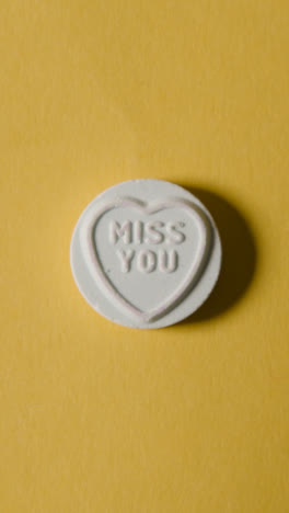 Vertical-Video-Close-Up-Of-Vertical-Video-Of-Hand-Holding-Heart-Candy-With-Dream-Girl-Message-On-Yellow-Background